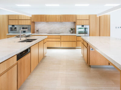 Cucina grande all'americana realizzata in legno chiaro, con top in marmo e due isole centrali.