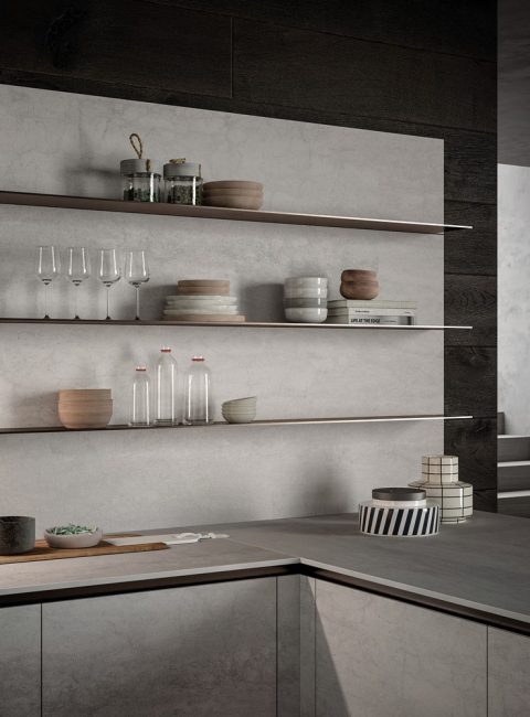 medium-E0_LAMINAM_PARTICOLARE-2 Vista della cucina con gola moderna e minimalista E0, con piani di lavoro color cemento chiaro e mensole in legno scuro.